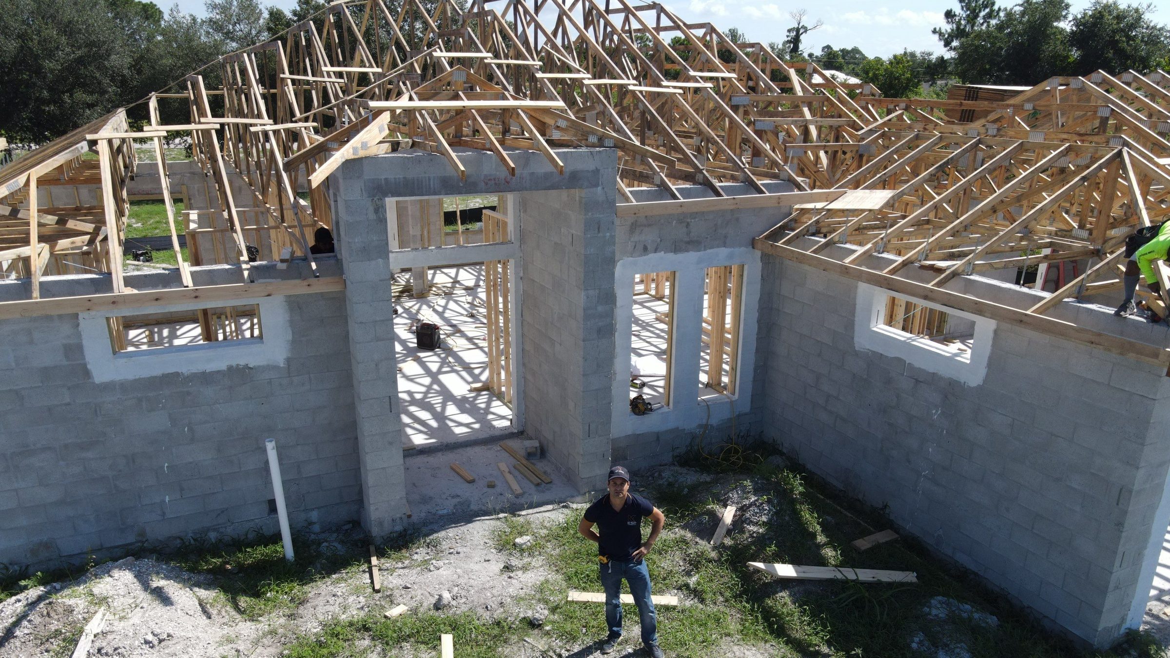 A KSP job site: concrete block walls, a poured tie beam and roof trusses going on, with Jimmy Saint Pere on site